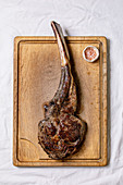 Grilled black angus beef tomahawk steak on bone served with pink salt on wooden cutting board over white cloth as background. Top view, space.