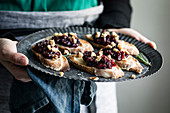 A woman holding a tray of cheese crostini with rosemary cranberry fig jam