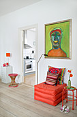 Sitzpouf in Orange unterm grünen Gemälde im Wohnzimmer