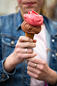 A hand holding strawberry and chocolate ice cream in a cone