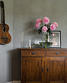 Candlestick and peonies on old cabinet next to guitar hung on grey wall