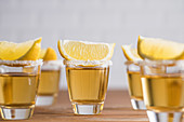 Glass sots with golden tequila and slices of lemon on wooden table
