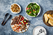 A platter of grilled meats with salad and baguette