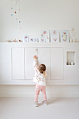 Kleines Mädchen am Wandschrank mit Babybildern