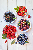 Various fresh berries in small bowls on a white wooden background