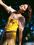 A young brunette woman wearing a summer outfit with a yellow top and a brown belt
