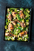 Satay chicken with green vegetables on a baking tray