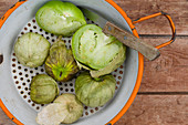 Green tomatillos in a strainer with a knife