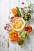 Hummus dip and raw vegetarian snacks on white wooden table