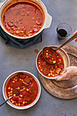 Overhead image of female hand serving tomato soup with chickpeas, chorizo sausage and parsley