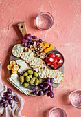 A cheese board with grapes, rosemary crackers, olives, stuffed mini peppers and walnuts