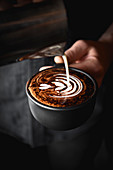 Barista giesst Milchschaummotiv auf Cappuccino