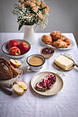 Bread with butter and jam, croissants, apples and coffee served for breakfast on a white linen tablecloth