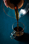 Tight image of coffee being poured from a pour-over pot into a glass mug
