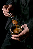 Young man in black shirt holding in hand bowl of homemade salted caramel sauce with spoon