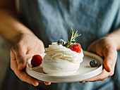 Woman hold plate with mini Pavlova cake decorated fresh berries and rosemary