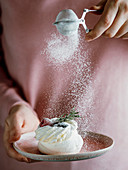 Woman holds plate with mini Pavlova cake with fresh berries, rosemary and icing sugar