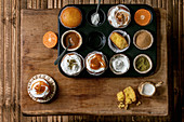 Homemade citrus oranges or clementines sweet muffins cupcakes in baked tray with different cream, pistachio, caramel toppings in bowls above on wooden table. Copy space