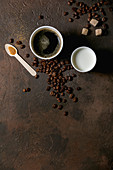 Kaffee im Pappbecher daneben Becher mit Milch, Kaffeebohnen und Löffel mit Zucker