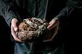 Man in black shirt holding in hands fresh baked artisan round homemade chocolate and cranberries rye bread.