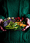 Hands holding a Buddha bowl with avocado, beetroot and kale