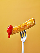 A chip dipped in tomato sauce on a fork against a yellow background