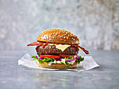 A beef burger with bacon against a light background in a sesame seed bun