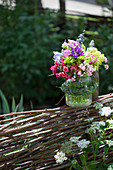 Blumenstrauß im Einmachglas mit Zopf aus Gras auf Flechtzaun gestellt