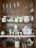 Glasses and vintage-style crockery in cupboard decorated with lace trim