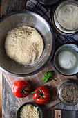 Pizza dough in a stainless steel bowl and ingredients for vegetarian pizza