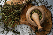 Getrocknete Minze im Olivenholz-Mörser und daneben auf Holzbrett auf Zeitungspapier