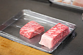 Wagyu beef on a metal tray covered with plastic wrap