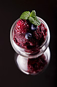 Berries sorbet in glasses. Summer refreshing dessert of raspberry, blueberry over on black background with reflection
