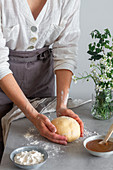 Anonymous female baker in apron kneading soft dough with flour on table