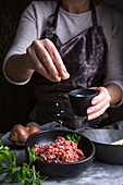 Anonymous female in apron spilling salt on fresh minced meat while preparing lunch