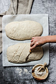 Cropped unrecognizable person hand cutting artisan bread loaf in a table dusted with white flour