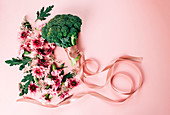 Bunch of pretty flowers and ripe broccoli with silk ribbon arranged on pink background