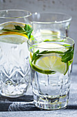 Various water glasses filled with lemons, limes, mint and ginger