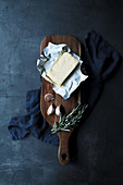 Opened pack of butter in composition with cloves of garlic and rosemary stems on wooden cutting board