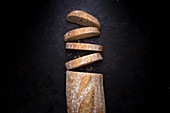 Pieces of fresh Italian bread with crunchy crust placed near loaf on black background