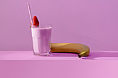Glass of delicious healthy dairy drink with fresh sweet strawberry and ripe banana on table in vivid purple light