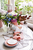 Geschirr, Gläser, Besteck und Hortensienstrauß auf Tisch am Fenster