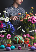 An Easter table laid with a Bundt cake, Easter eggs and flowers with a woman in the background
