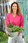 A young woman with a bowl of fresh herbs wearing a pink jumper