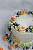 A cream cheese cake decorated with kumquats, blueberries and flowers