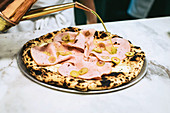 Olivenöl wird auf Pizza Bianca mit Mortadella geträufelt