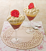 Two dessert trifles in tall stemmed glasses, with piped cream and a rasberry crisp