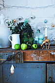 Eucalyptus branches in jug, green apples, glass cover and candle stick on top of old cupboard