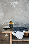 Handtücher, Flasche und Schale mit Seifen auf Holzbank