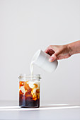Iced Coffee: Milch wird in Glas mit kaltem Kaffee gegossen